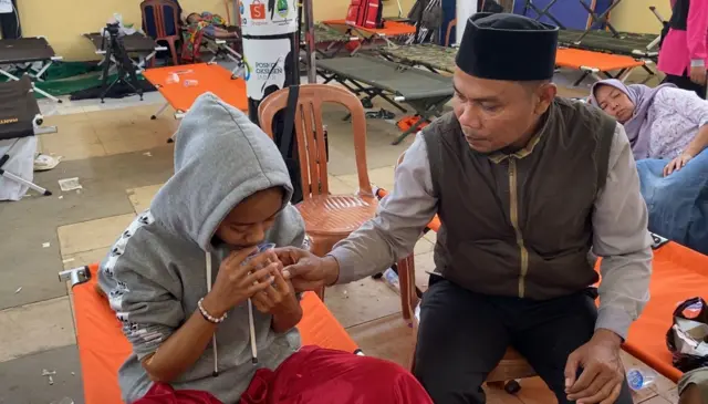 Seorang pria sedang membantu memberi minum pada anak perempuan.