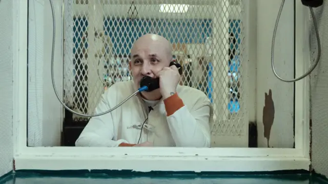 César Fierro en la cárcel en Texas. Está sentado detrás de un cristal y sostiene un teléfono por el que habla con el director Santiago Esteinou.