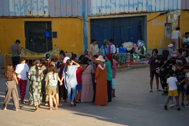 Un grupo de personas, entre ellas varios niños, se reúnen junto a un edificio industrial en Ceuta. 