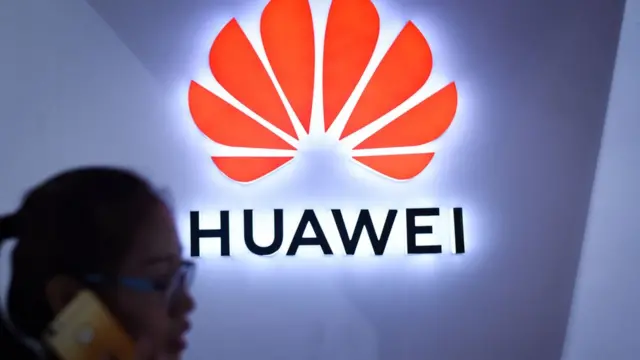 A woman uses a phone in front of Huawei logo