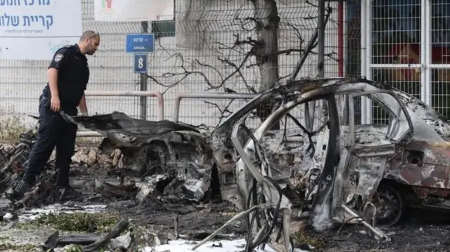 ইরানের ব্যালিস্টিক ক্ষেপণাস্ত্র হামলার পর তেল আভিভে পুড়ে যাওয়া গাড়ি পরিদর্শন করছেন একজন ইসরায়েলি পুলিশ