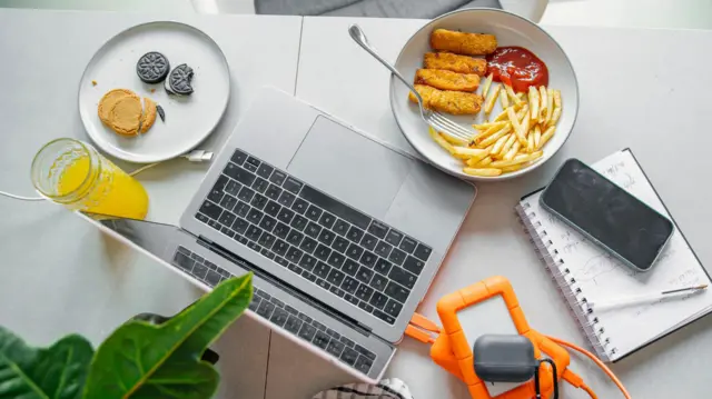 Laptop'a tepeden bakan görselde nugget, patates kızartması ve bisküviler gibi aşırı işlenmiş gıdalar var.