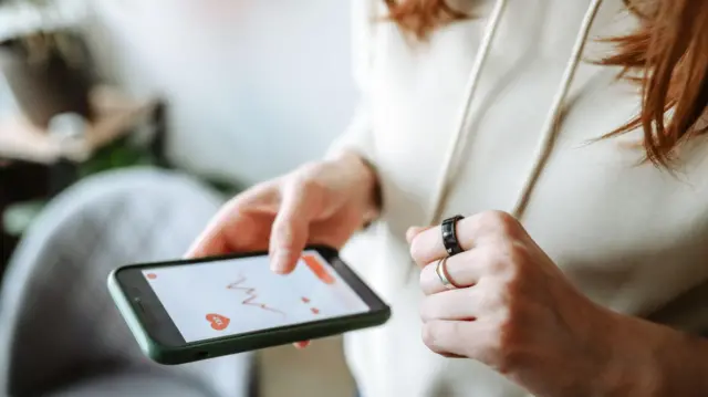 Mulher usando um anel inteligente e verificando seus dados de saúde no aplicativo de celular