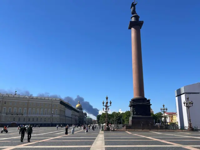 Дворцовая площадь в Петербурге, вид на Александровскую колонну, виден купол Исаакиевского собора, а за ним дым.