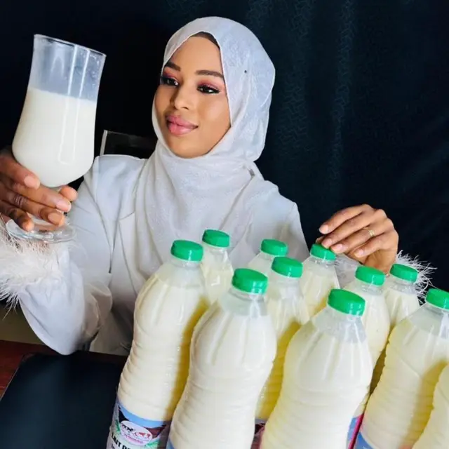 Madipa avec plusieurs bouteilles de lait frais et un vers de lait en main.