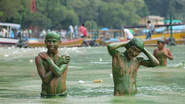 Jovens tomando banho no lago Amatitlán, cobertos pela alga verde