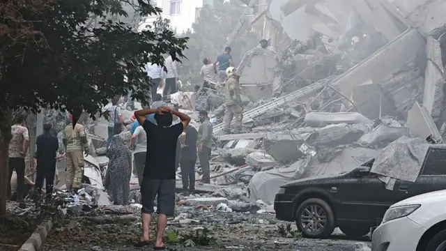 Pessoas observam os danos a prédios na Praça Nobonyad após os ataques aéreos israelenses em 13 de junho de 2025 em Teerã, Irã