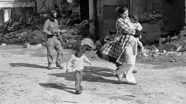 امرأة وولديها وخلفهما مسلح في بيوت خلال الحرب الأهلية