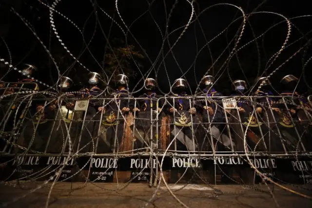 Riot police stand guard behind barbed wire road block during an anti-government protest in Bangkok, Thailand, 21 October 2020.