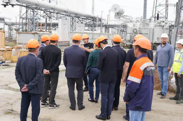 Чоловіки в костюмах і помаранчевих робочих касках на енергетичній підстанції 