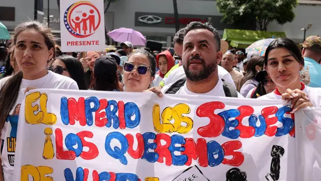 Quatro pessoas carregam uma faixa de protesto. Todos estão vestindo camisetas brancas.