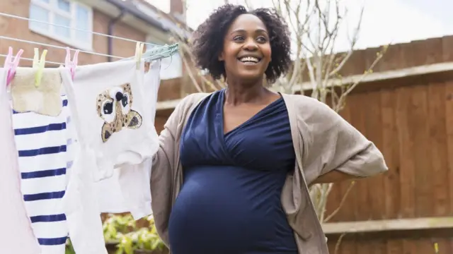 Une femme enceinte heureuse étend du linge sur une corde à linge dans un jardin.