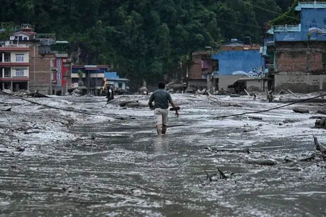 Um morador caminha por uma rua coberta de lama após enchentes repentinas e um deslizamento de terra em Devighat, no distrito de Nuwakot, no Nepal, em 26 de agosto de 2026
