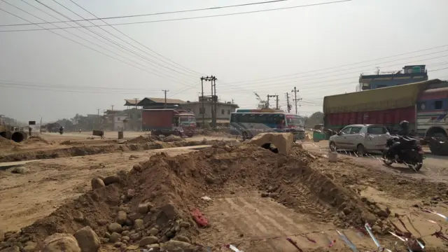 निर्माणाधीन सडकमा थुप्रिएको माटो र छेउमा गुड्दै गरेका सवारीसाधनहरू