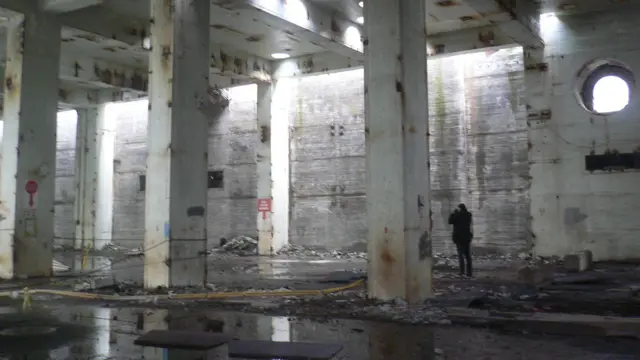 Pessoa tirando fotografias em um edifício vazio de altas colunas na central nuclear de Lemóniz, na Espanha