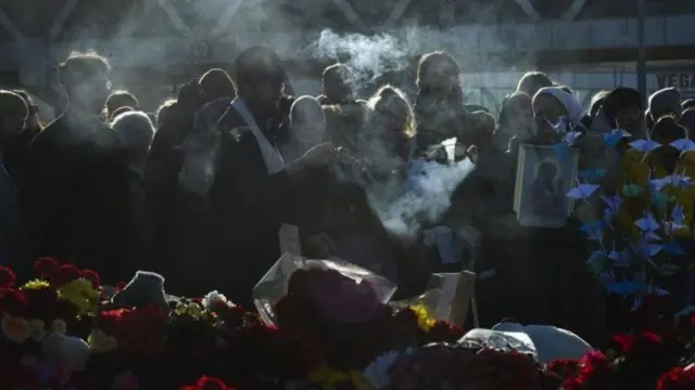 Mourners gather alongside flowers