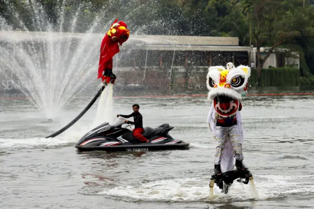 Люди в традиционных костюмах для Танца льва поднимаются на шланге, выпускающем струю воды
