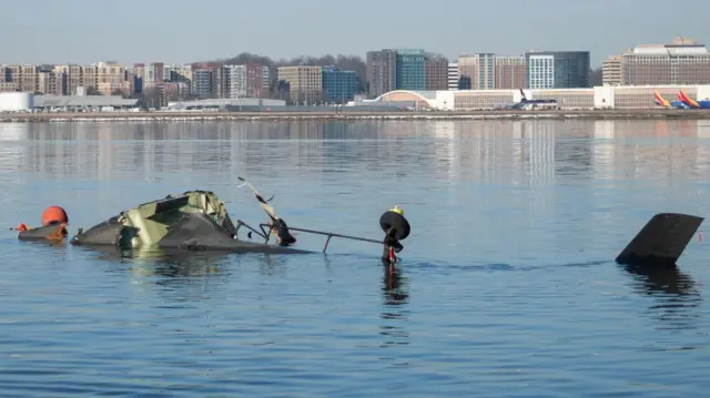 Обломки вертолета торчат из воды, вдали на заднем плане на противоположном берегу реки - многоэтажные здания