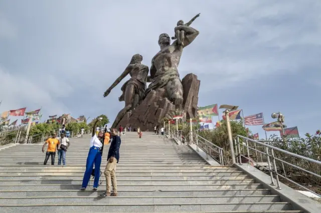 Des touristes prennent des photos devant le Monument de la Renaissance, qui symbolise la solidarité et l'avenir radieux des pays du continent africain contre le colonialisme des pays occidentaux, à Dakar, au Sénégal, le 21 juillet 2022. Ce monument en bronze de 52 mètres de long et pesant 7 000 tonnes représente une famille africaine émergeant d'un volcan.