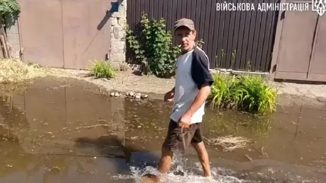 Seorang pria menerabas banjir di Kherson - sebuah kota yang terletak di tepi barat Dnipro.