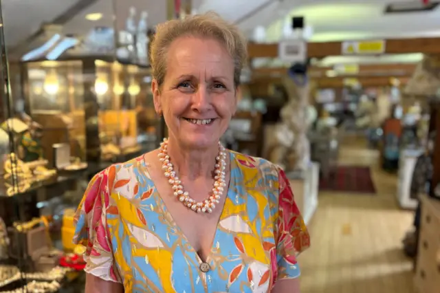 Леслі Остін посміхається в камеру. У неї коротке світле волосся, вона одягнена в різнокольорову сукню з намистом.