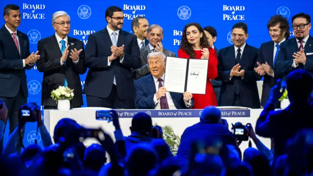 Donald Trump holds a signed founding charter at the Board of Peace meeting during the 56th annual meeting of the World Economic Forum in Davos, Switzerland on 22 January 2026. Politicians from around the world are standing behind him, several of them clapping