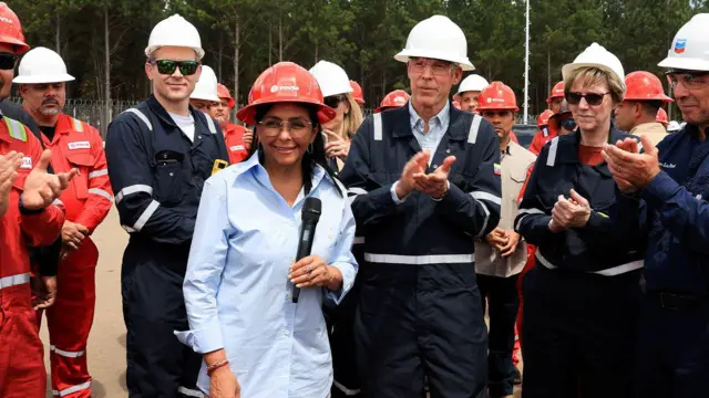 Venezuela'nın geçici Cumhurbaşkanı Rodríguez ve ABD Enerji Bakanı Chris Wright petrol tesislerini geziyor. Rodriguez, turuncu baret ve açık mavi gömlek giymiş, solda duruyor. Chris Wright ise beyaz baret ve mavi tulum giymiş.