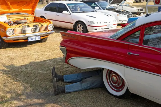 Ƙafafu biyu sanye da shuɗin wandon Jeans a ƙarƙashin wata daɗaɗɗiyar mota, a wajen bikin baje kolin tsaffin motoci masu ƙayatarwa a birnin Sasolburg na Afirika ta Kudu a ranar 31 ga watan Ogustan 2025.