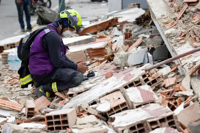 Un rescatista con casco, tapabocas y chaleco morado usa un dispositivo de detección de sonido sobre los escombros de un edificio en Catia La Mar, Venezuela.