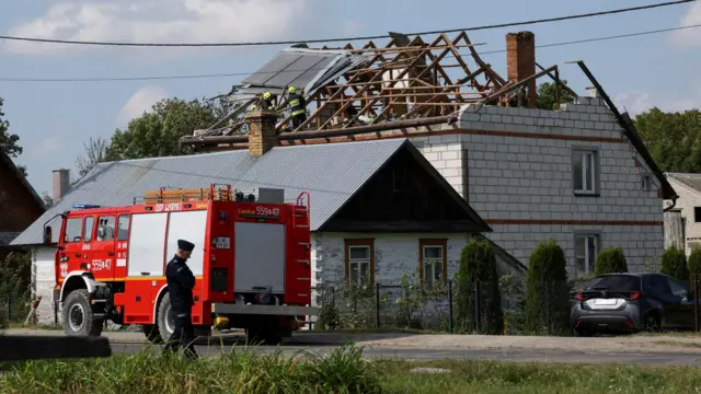 Красная пожарная машина стоит около белого кирпичного дома с разрушенной крышей