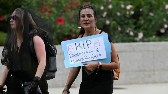 プラカードを手にした女性は、喪服のように黒いベールを顔につけている。隣にいる女性も黒衣を身に着けている 