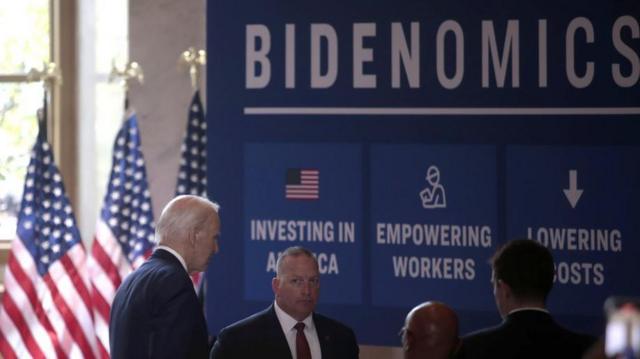 Biden e assessores pertomega sena 2484 caixa economica federalbandeiras dos EUA e painel com a palavra 'Bidenomics'