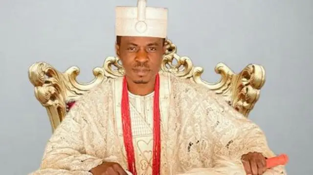 Ọba Ayodeji Williams Adesoye wọ agbada at sokoto asọ leesi alawọ miliki, o de ade alawọ miliki bakan naa, o si fi ọpọlọpọ ilẹkẹ iyun sọrun, o tun mu irukẹrẹ funfun kan dani lọwọ alaafia.