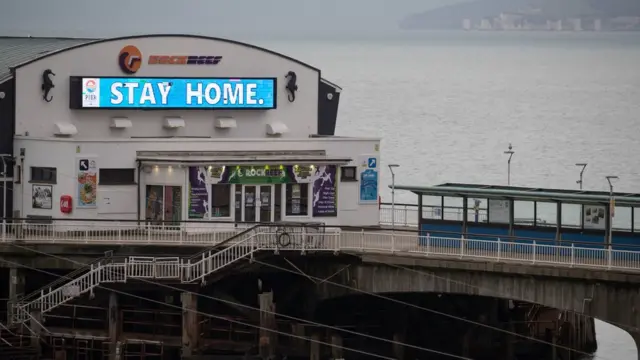 вывеска "оставайтесь дома" на пирсе в Борнмуте