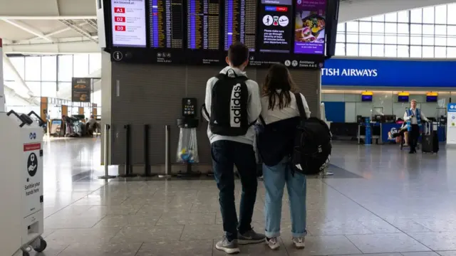 Unos pasajeros viendo las pantallas de vuelos en el Terminal 5 del aeropuerto londinense de Heathrow