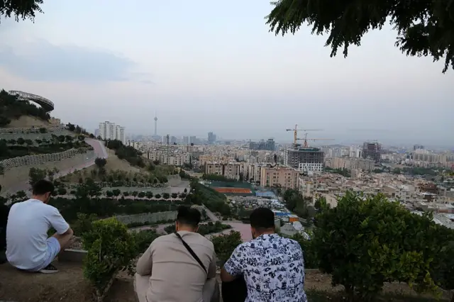 سه مرد از پشت سر بر بلندی مشرف به تهران نشسته‌اند