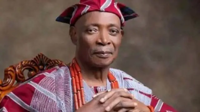 Olubadan Rashidi Ladoja wọ agbada toke tilẹ asọ oke alaari ati fila rẹ, fi ilẹkẹ iyun mẹta sọrun, o so ọwọ rẹ pọ, o n wo ọkankan