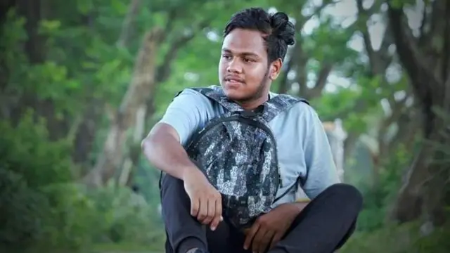 画面中可以看到一位黑发青年背着背包坐在树前。