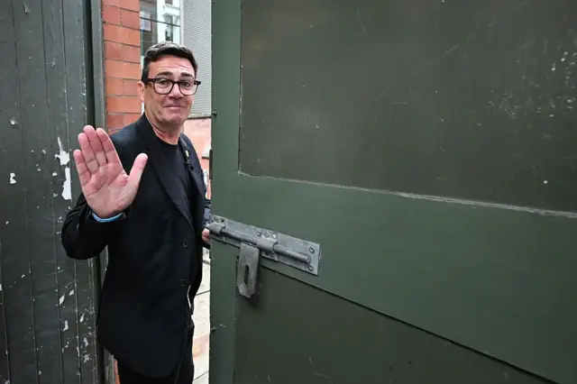 Wearing a black suit and T-shirt, Andy Burnham waves goodbye as he leaves the People's History Museum, in Manchester, UK, after delivering a speech, on 29 June 2026. 