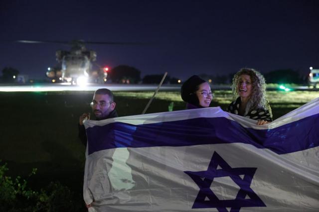 3 pessoas sorrindo e segurando bandeiraestrategia futebol virtual betanoIsrael, com helicóptero ao fundo