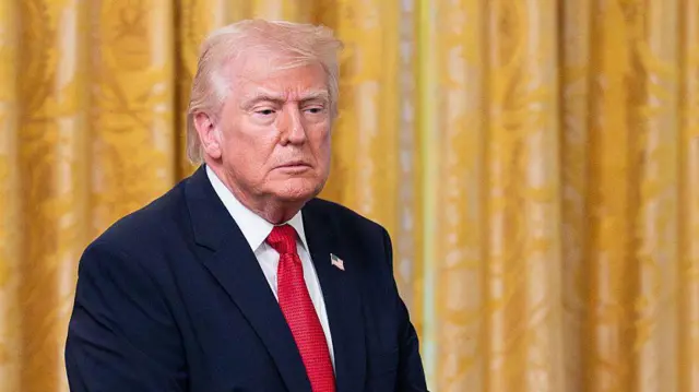 Trump amejifunga tai nyekundu na koti ya suti dhidi ya pazia la rangi ya dhahabu