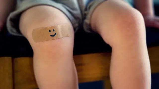 一只幼童的双脚，其中一个膝盖上贴上画有笑面的胶布。