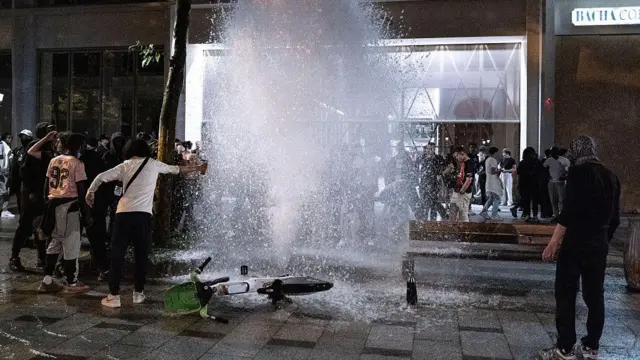 Un grupo de hombres alrededor de un chorro de agua que sale de un hidrante roto.