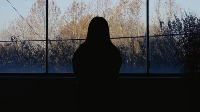一名女子凝视窗外的剪影,背景为树木与绿意。