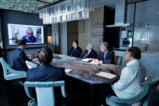 အမျိုးသားညီညွတ်ရေးအစိုးရ (NUG) ဝန်ကြီးချုပ် မန်းဝင်းခိုင်သန်းကို တီဗီဖန်သားပြင် ပေါ်မှာ စကားပြောနေတာတွေ့ရပြီး မြန်မာနိုင်ငံဆိုင်ရာ မလေးရှား အထူးကိုယ်စားလှယ် အပါအဝင် အမျိုးသား ၆ ဦးက အဲဒီ ဖန်သားပြင်ဘက်လှည့်ပြီး နားထောင်နေကြ။ အမျိုးသား ခြောက်ဦးစလုံးဟာ စားပွဲဝိုင်းအရှည်တစ်ခုမှာ ထိုင်ခုံတွေနဲ့ ထိုင်နေကြတာဖြစ်ပါတယ် 