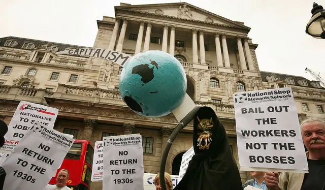 Uma figura da Morte segura um globo terrestre atravessado por uma foice em frente ao Banco da Inglaterra durante um protesto em 13 de outubro de 2008 em Londres