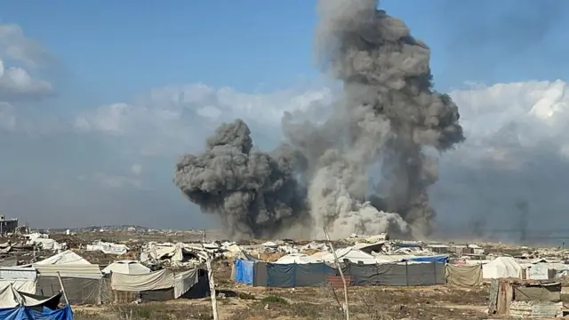 الصورة التقطت نهاراً حيث يظهر دخان ناجم عن القصف خلف الخيام.