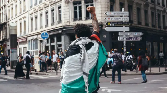 Homem ergue braço, envolto por bandeira palestinablaze site de apostas onlinerua francesa 