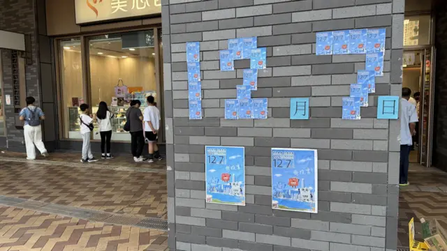 香港元朗洪水桥洪福邨商场一面墙上贴上了以小张12月7日立法会选举投票官方宣传海报堆砌成的“12月7日”字样(BBC中文图片16/11/2025)