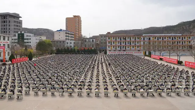 2015年4月11日,中國陝西省延安市宜川中學逾1,700名學生在學校操場上參加戶外考試。大批學生坐在排列整齊的課桌前應試,桌椅分布於寬闊的操場上。學生之間保持一定距離,場面規模龐大。背景可見操場設施、校園建築及周圍環境,展現大規模集體考試的場景。